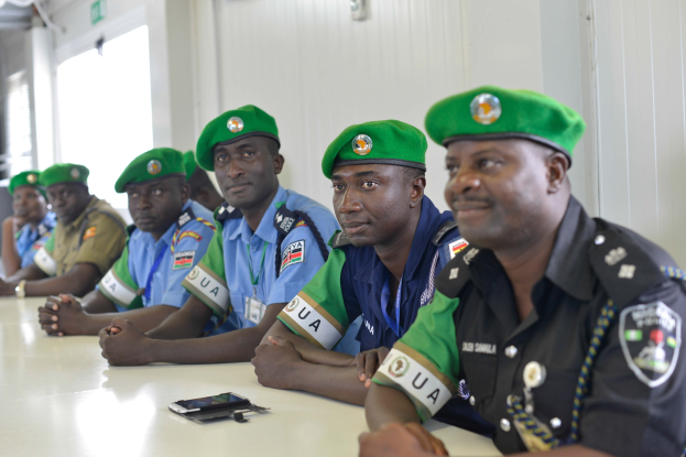 Gruppe von Polizisten bei einer Schulung an einem Tisch sitzend, mit Mobiltelefonen und anderen Gegenständen auf dem Tisch, in einem Raum mit Fenstern und Deckenbeleuchtung.