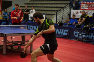 Eine Gruppe von Menschen in verschiedenen Farben, darunter schwarz, weiß und blau, sitzt um einen Tisch mit einem Spiel im Hintergrund, mit Stühlen und einer Treppe.