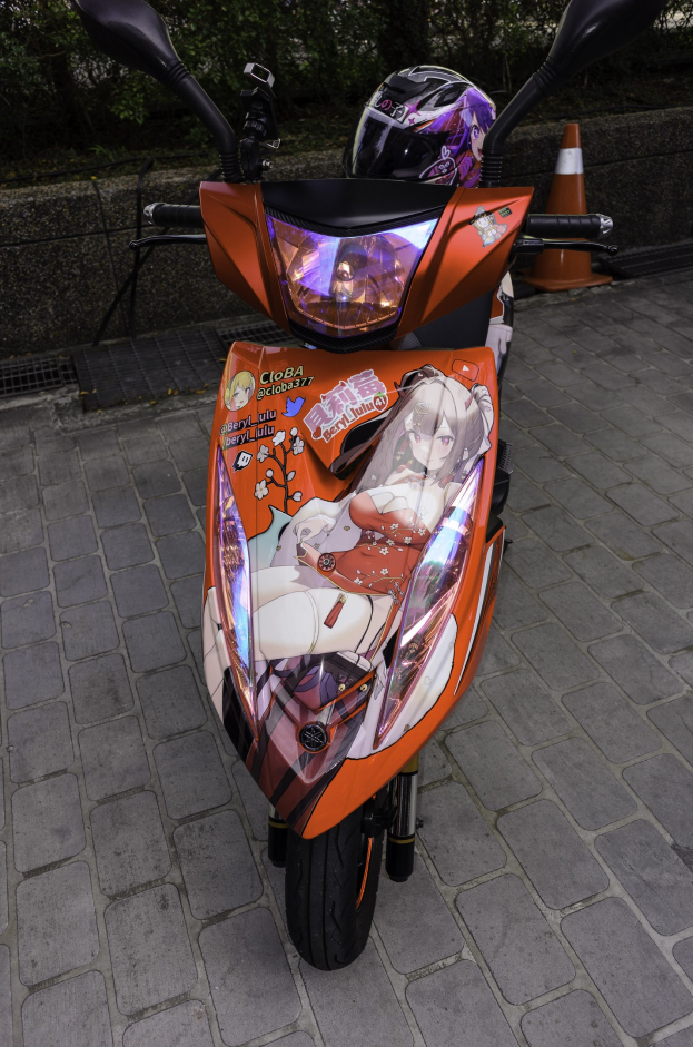 Ein oranger Roller auf der Straße geparkt mit einem Helm daneben, neben einem Verkehrskegel, einer Wand und Bäumen im Hintergrund.