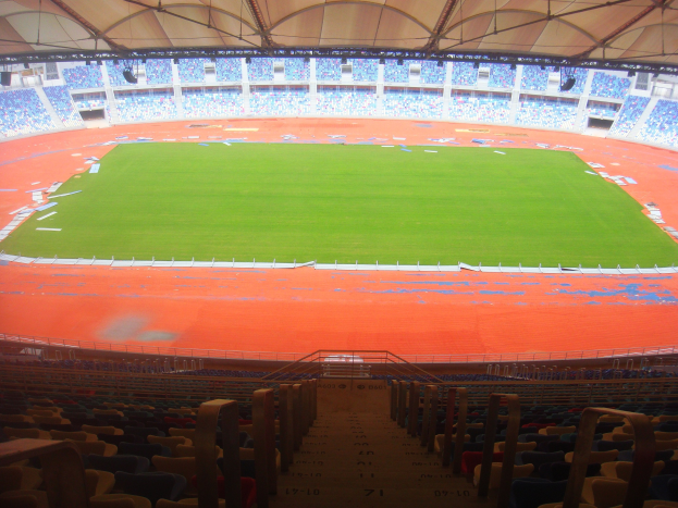 Großes Stadion mit vielen Zuschauern, mit Sitzreihen, Geländern, Treppen und Dach, mit sichtbarem zentralem Feld.