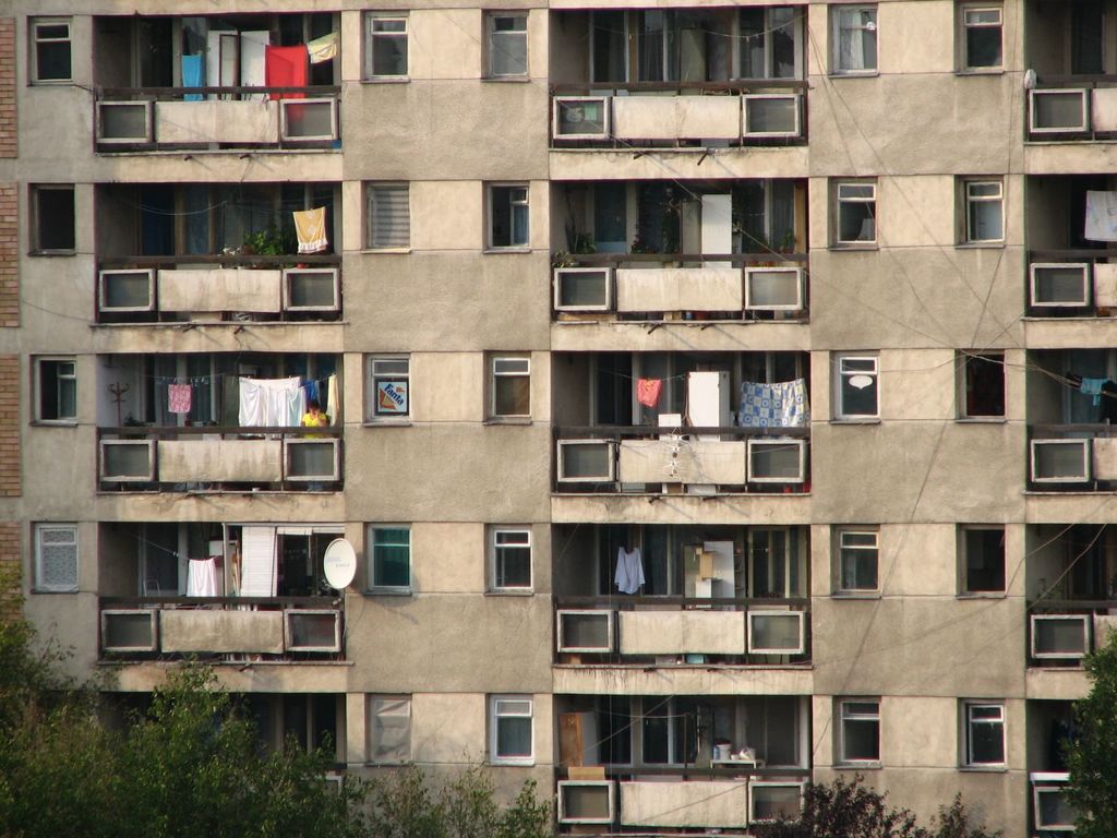 Ein mehrstöckiges Gebäude mit Balkonen, Wäsche an Seilen, eine Parabolantenne und Baumzweige mit Blättern unten.