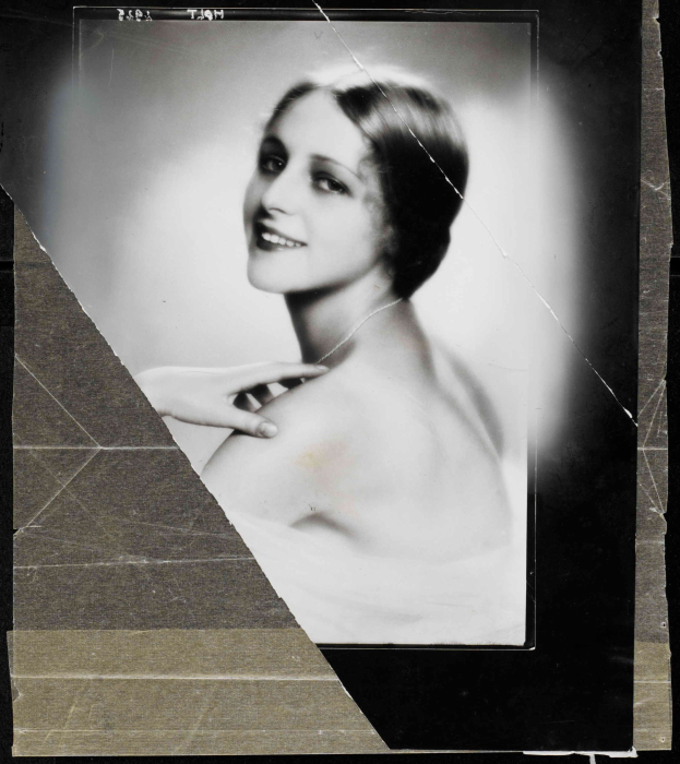 Schwarz-weiß-Porträt einer Frau in einem Kleid im Stil der 1920er Jahre mit einem ordentlichen Dutt, die warm in die Kamera lächelt.