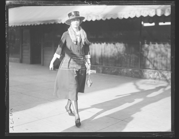 Frau in einem Kleid und Hut, die die Straße entlang geht und eine Handtasche trägt, hohe Absätze trägt, in Schwarz-Weiß.