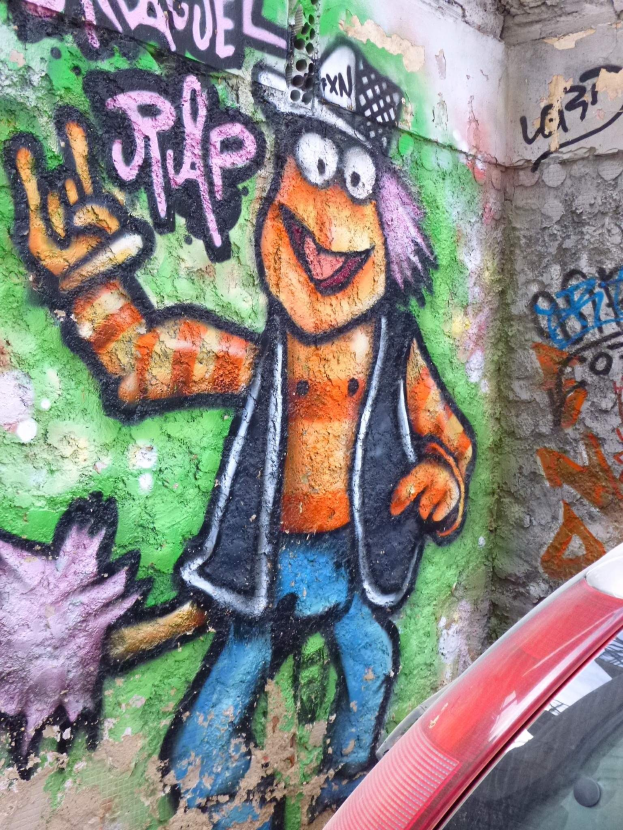 Ein rotes Auto, das vor einer bunt bemalten Graffitiwand geparkt ist.