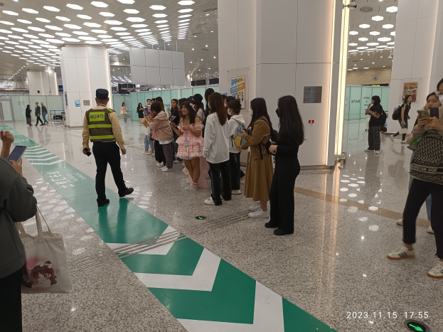 Menschen in der Warteschlange an einem Flughafen-Sicherheits-Check-in-Bereich mit Taschen und Mobiltelefonen, mit Säulen und Deckenleuchten im Hintergrund.