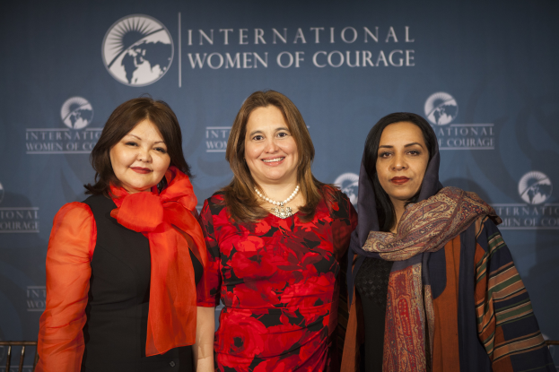 Drei Frauen, die vor einem Banner mit der Aufschrift "Internationale Frauen des Mutes" zusammenstehen und lächeln.