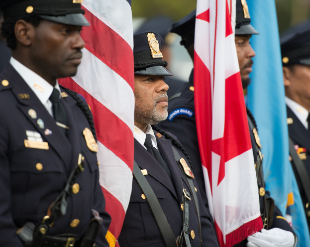 Eine Gruppe von Polizisten in Uniform und mit Mützen, die zusammen stehen und Fahnen halten, vor einem unscharfen Hintergrund.