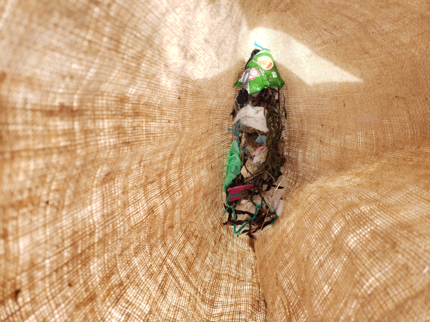 Nahaufnahme eines zerknüllten Papierstücks auf einem Tisch mit einem Jutestoff im Hintergrund, wahrscheinlich recycelter Abfallmaterial.