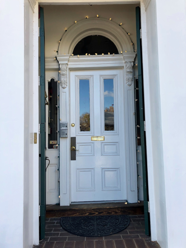 Ein weißes Haus mit einer blauen Tür, einem Türvorleger und dekorativen Lichtern an der Tür.