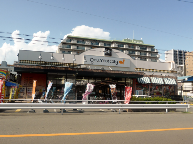 Eine belebte Stadtstraße mit Gebäuden, Straßenlaternen, Werbetafeln, Fahrzeugen, Absperrgittern, Büschen, Bäumen und einem bewölkten Himmel, in dessen Mitte ein Gourmetrestaurant verschiedene Speisen anbietet.