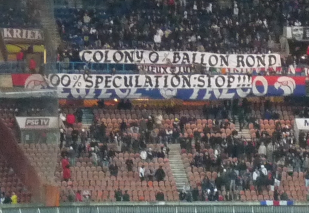 Ein Stadion voller Menschen, Fahnen und Stühle, mit einem Zaun unten und Treppen auf der linken Seite.