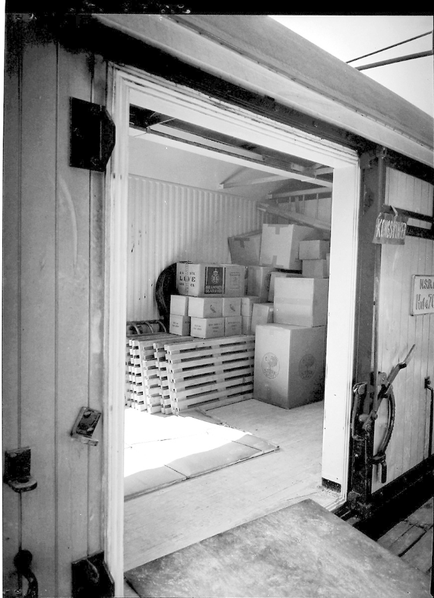 Schwarz-weiß-Foto eines metallenen Seecontainers mit einer Tür auf der linken Seite, gefüllt mit ordentlich gestapelten Kartons.