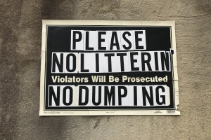 Schwarzes und weißes Schild an einem Gebäude mit der Aufschrift "Bitte keine Verschmutzung Verursacher werden strafrechtlich verfolgt Keine Ablagerung".