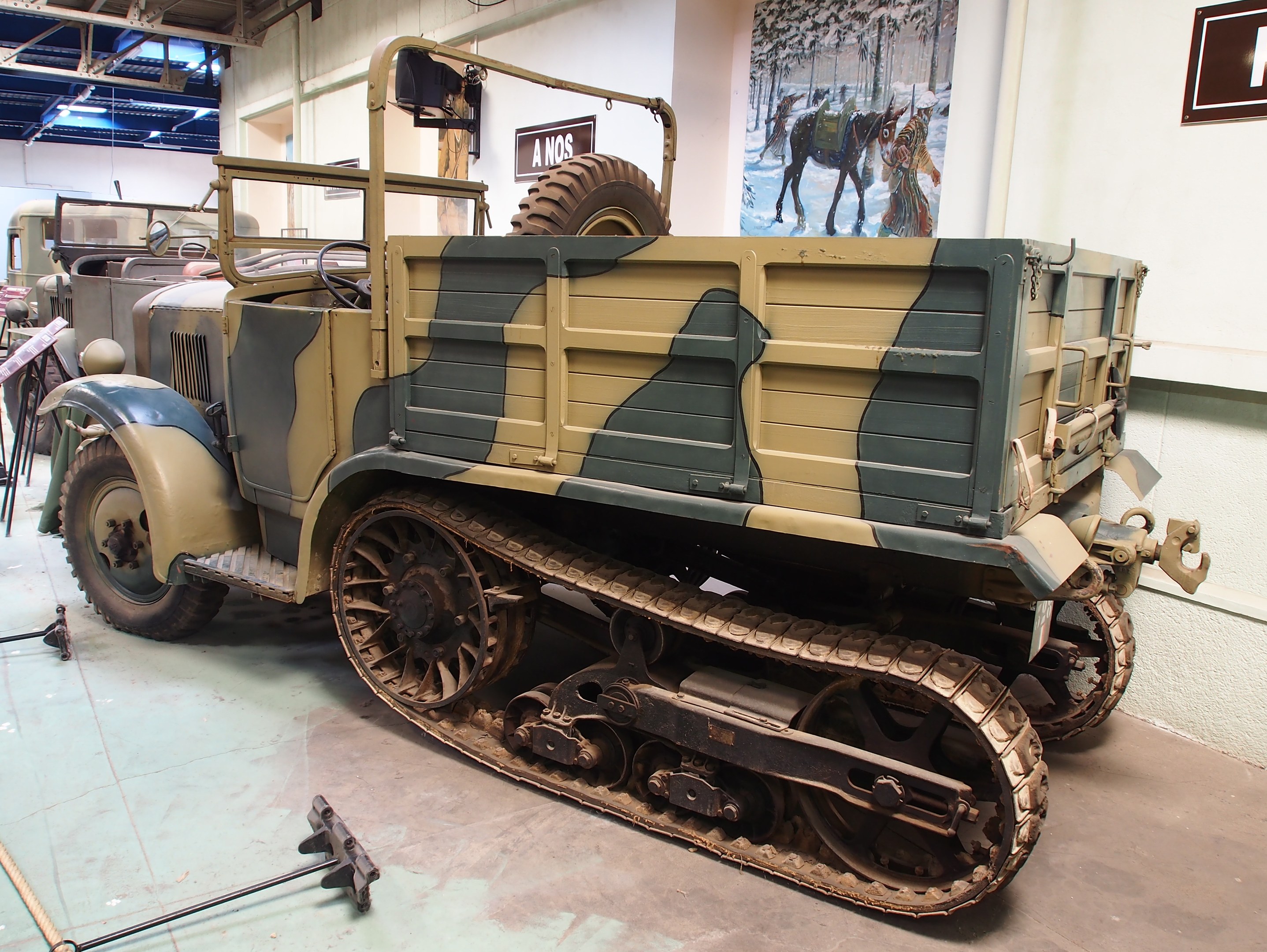 Ein militärisches M3A1-Spähwagen-Fahrzeug im Museum ausgestellt, umgeben von anderen Fahrzeugen und Ausstellungsstücken.