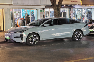 Ein Mitsubishi Lancer EV auf einer städtischen Straße bei Nacht geparkt, umgeben von Gebäuden, beleuchteten Schaufenstern, Schaufensterpuppen in Kleidern und verschiedenen Schildern.