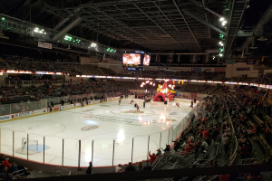 Ein Eishockeyspiel im Columbus Blue Jackets Stadion mit Zuschauern auf Sitzen und Stehplätzen, einem eingezäunten Eis, Bannern und Überwachungsbildschirmen und -leuchten.