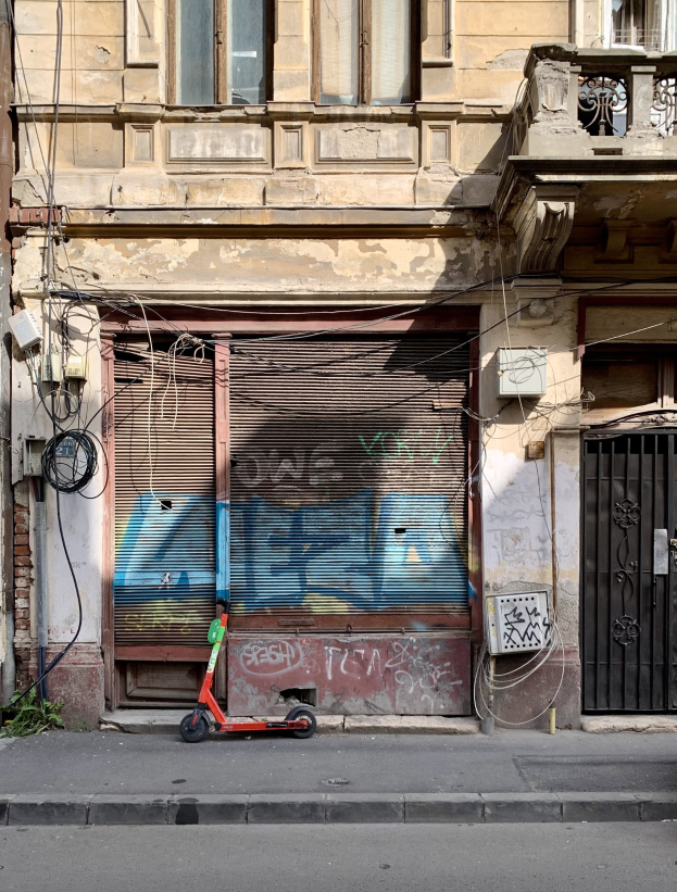 Ein roter Roller neben einem Gebäude mit Fenstern, Läden und einem Tor auf einer Straße mit sichtbaren Kabeln und anderen Gegenständen.