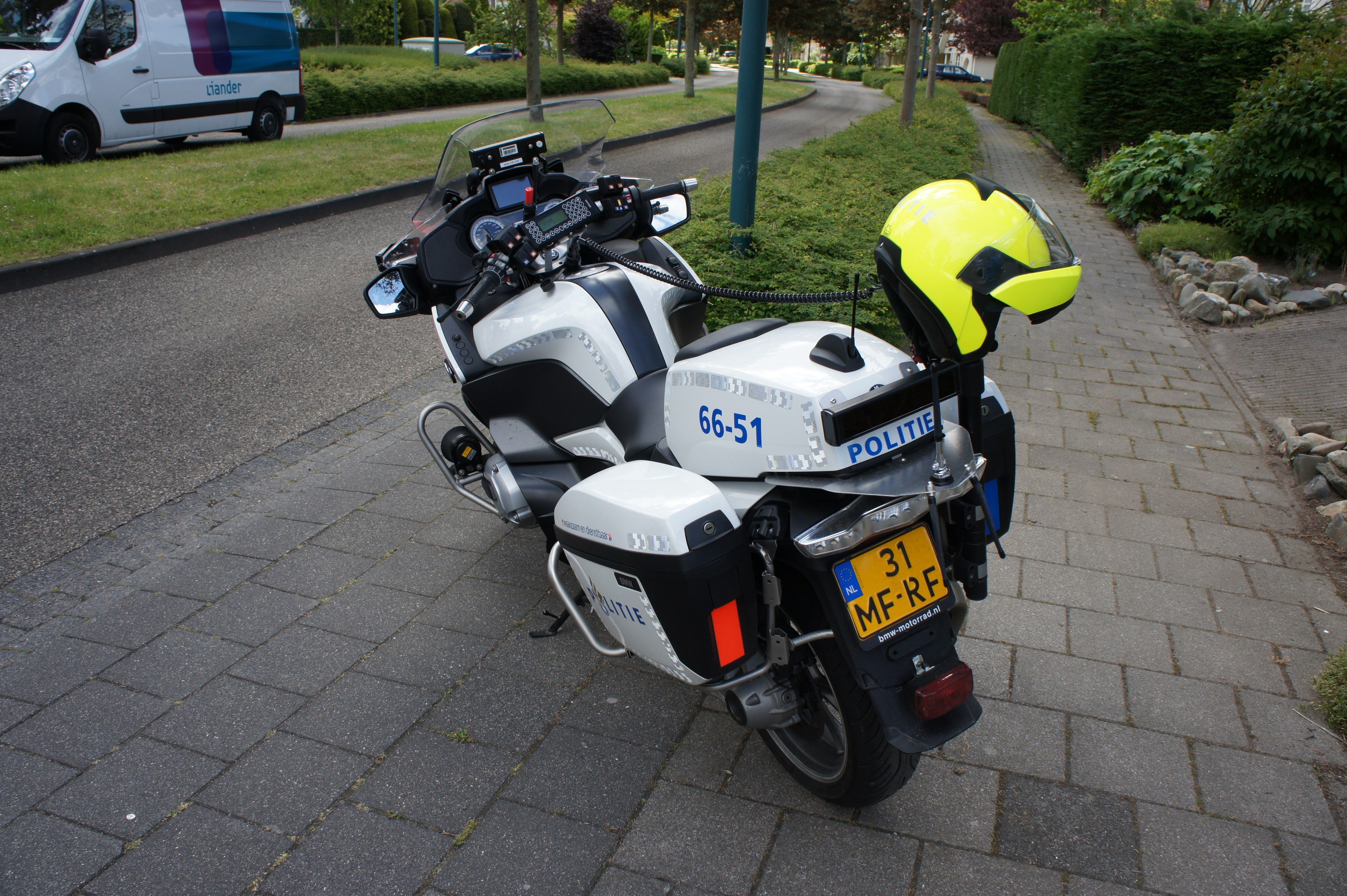 Polizeimotorrad am Straßenrand geparkt mit einem Helm darauf, Bäume und Gebäude im Hintergrund.