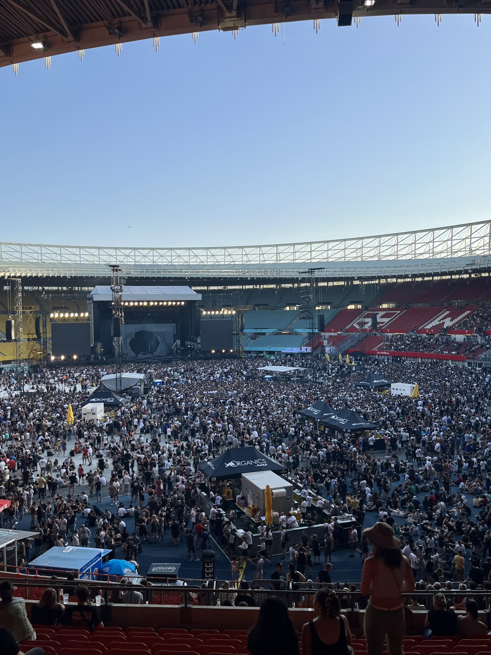Große Menschenmenge auf Sitzplätzen und Stehplätzen in einem Stadion mit Geländern, Zelten und Überdachung während eines Events in der O2 Arena in London.