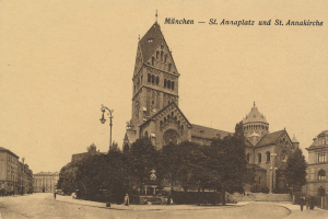 Schwarz-weiß-Foto einer Stadtstraße mit Gebäuden, Bäumen, Straßenlaternen, Autos, Menschen auf dem Gehweg, Statuen und einem Himmel im Hintergrund. Text oben lautet "München - St. Annaplatz und St. Annakirche".