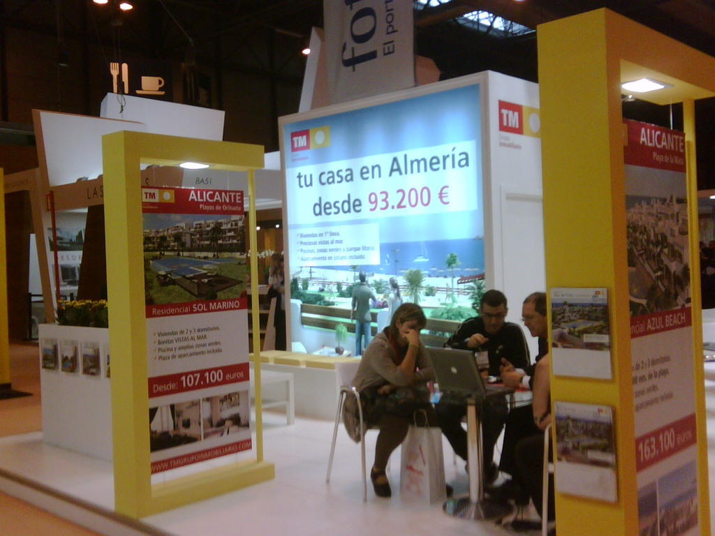 Eine Gruppe von Menschen sitzt an einem Tisch und schaut auf einen Laptop, mit mehreren Flyern, auf denen verschiedene Anzeigen zu sehen sind.