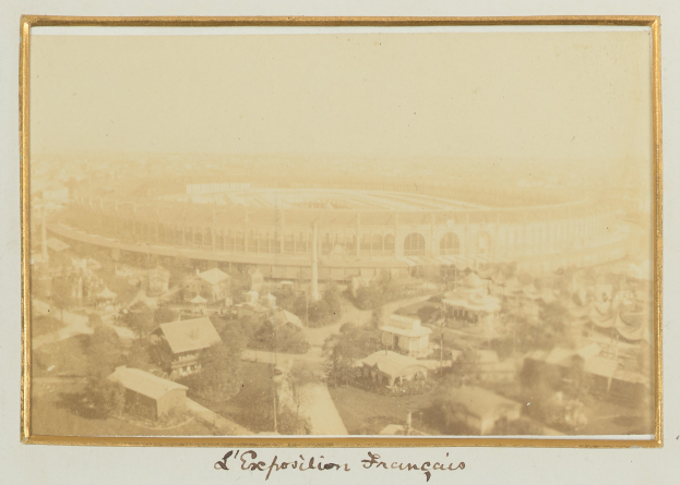 Altes Foto eines Stadions in einer städtischen Umgebung mit umliegenden Gebäuden, Bäumen und Pfählen, mit Text unten.