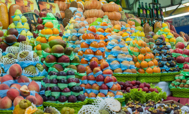 Ein Marktstand mit Äpfeln, Orangen, Birnen und anderen Obst und Gemüse, mit Flaschen auf Regalen und Deckenbeleuchtung.