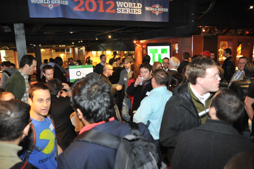 Eine große Menschenmenge versammelte sich bei einem Ereignis mit einem Bildschirm, der ein Bild anzeigt, Lichtern und einer hölzernen Wand im Hintergrund.