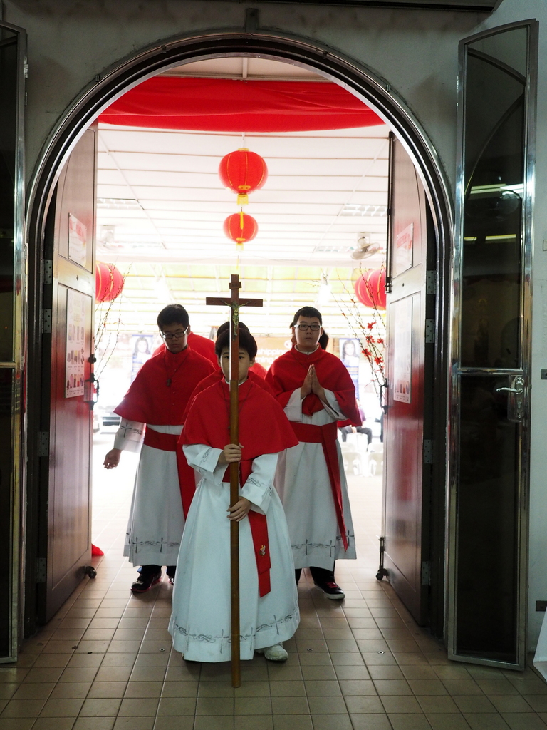 Menschen, die in einer Kathedrale gehen und ein Kreuz halten, mit Türen auf beiden Seiten und Blumen im Hintergrund.