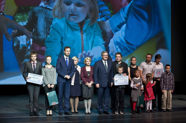 Gruppe von Menschen auf einer Bühne mit Taschen und Urkunden, Hintergrundbild mit einem Kind und anderen Personen