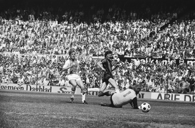 Schwarzes Foto von Füßballspielern in Aktion auf einem Feld mit Zuschauern im Hintergrund und einer Bundesliga 1978-79 Ajax 1-1 Hannover 96 Fahne.
