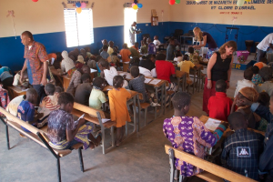 Kinder auf Bänken in der Nähe mit Erwachsenen, die sie führen, Stühle, eine Tür, ein Fenster und ein Tisch in der Ferne, Ballons und Text oben.
