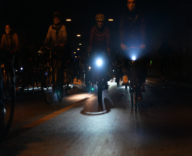 Eine Gruppe von Menschen, die nachts mit Fahrrädern auf einer Stadtstraße fahren und Helme tragen.