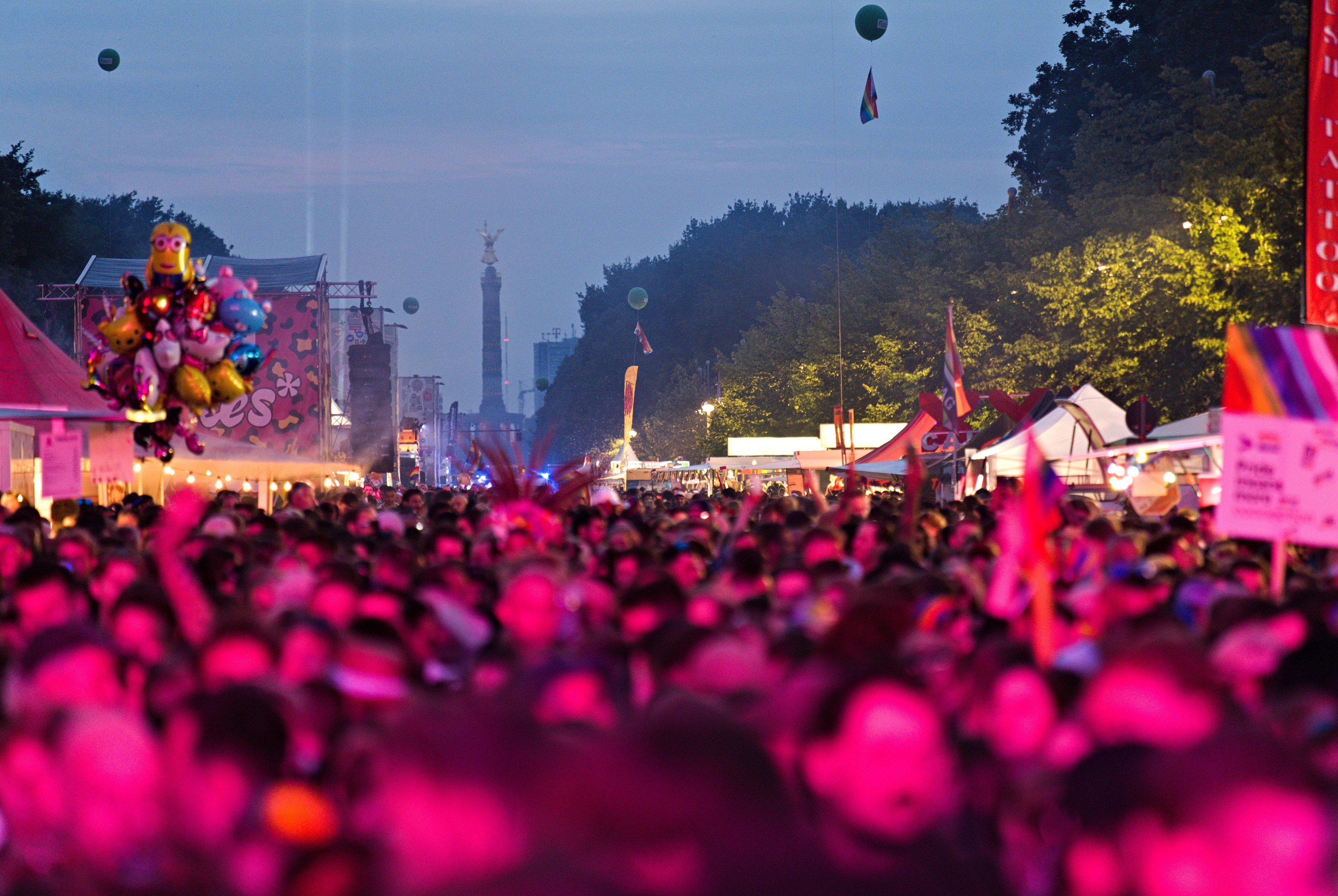Eine große Menge Menschen auf einem nächtlichen Musikfestival mit bunten Lichtern, Ballons, Zelten, Bannern, Fahnen, Bäumen, einem Turm und einem sternenklaren Himmel im Hintergrund.