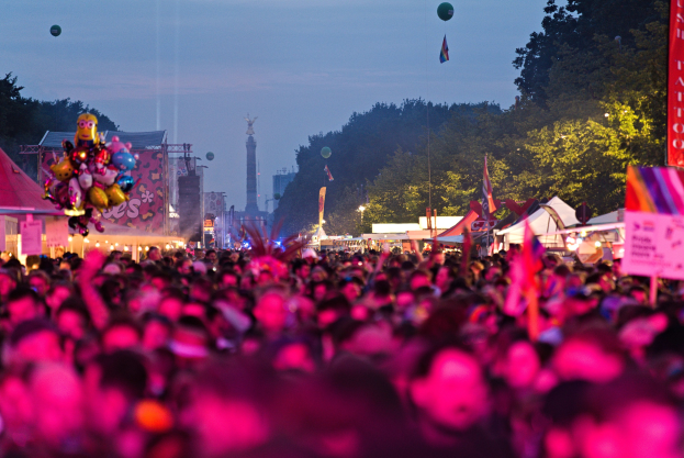 Eine große Menge Menschen auf einem nächtlichen Musikfestival mit bunten Lichtern, Ballons, Zelten, Bannern, Fahnen, Bäumen, einem Turm und einem sternenklaren Himmel im Hintergrund.