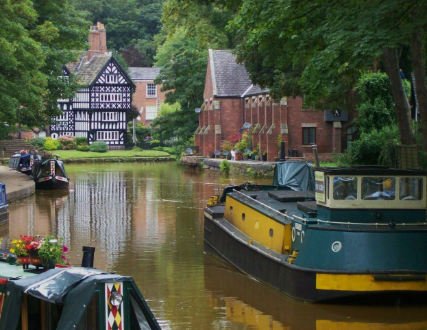 Ein von Booten gesäumter Kanal, umgeben von Grün und Bäumen, mit Gebäuden im Hintergrund.