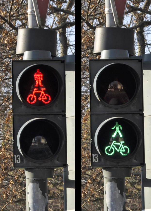 Verkehrsampel zeigt sowohl rote als auch grüne Ampel, vor Wald und einem klaren blauen Himmel.