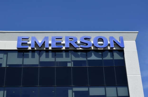 Emerson-Logo an einer Gebäudefassade mit dem Text "Emerson investiert 1,5 Milliarden US-Dollar in den USA" vor einem klaren blauen Himmel.