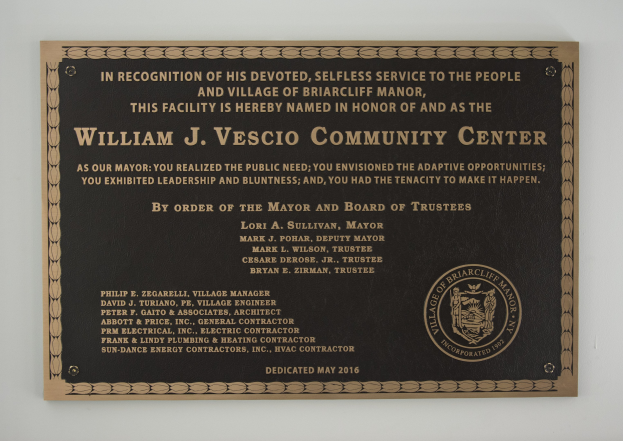 Schwarzes rechteckiges Schild mit weißer fettgedruckter Schrift, die "William J. Vesco Community Center" lautet, angebracht an einer Gebäudewand.