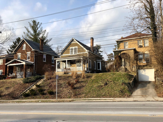 Reihe von Häusern entlang einer Straße mit Fenstern, Türen, Säulen, Geländern, Stufen, Pflanzen, Gras, Bäumen und einem Pfahl mit einer Tafel, unter einem bewölkten Himmel, repräsentiert eines der teuersten Häuser zum Verkauf in Detroit.