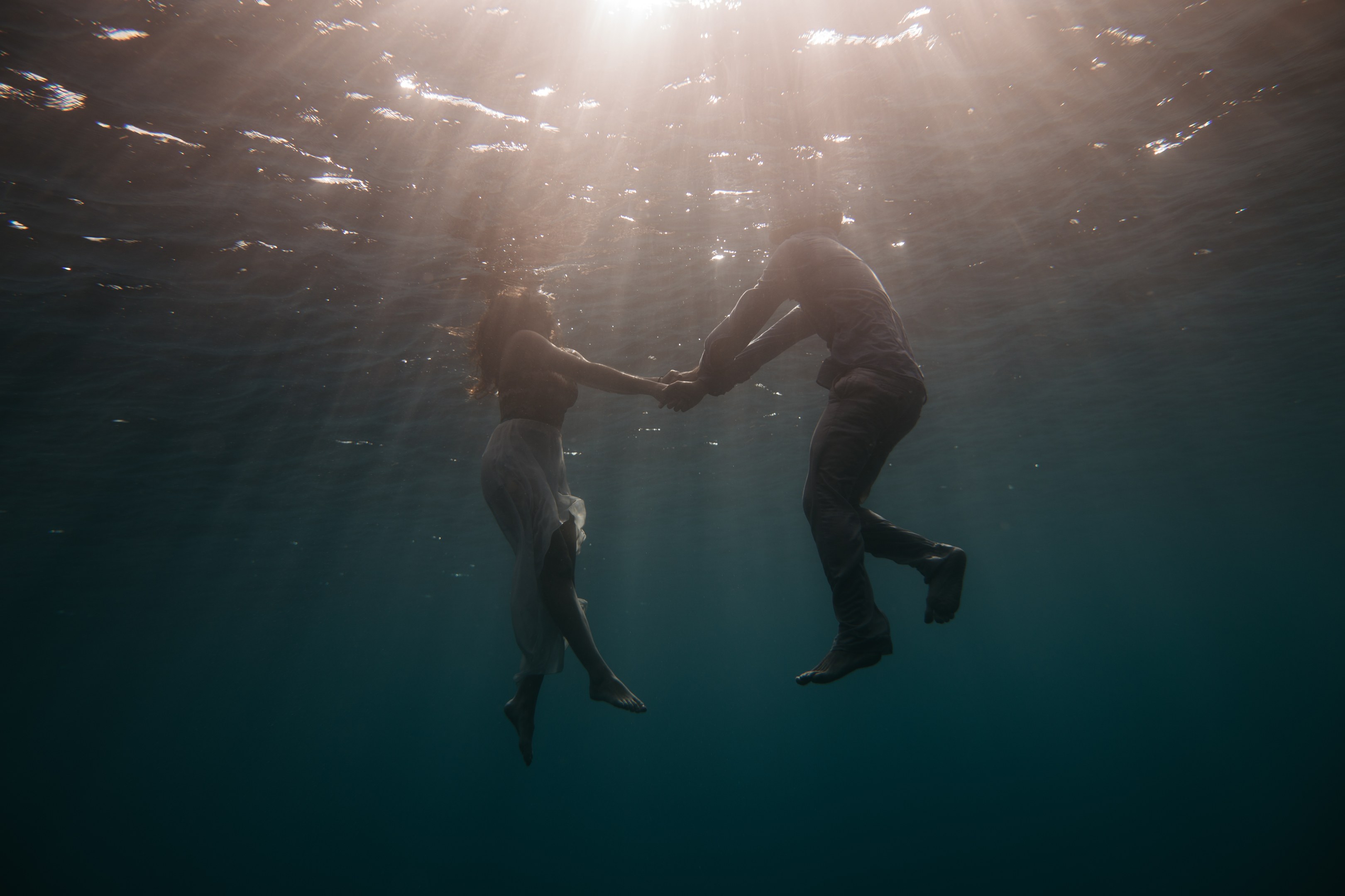 Zwei Personen halten sich unter Wasser in der See mit einfallenden Sonnenstrahlen.