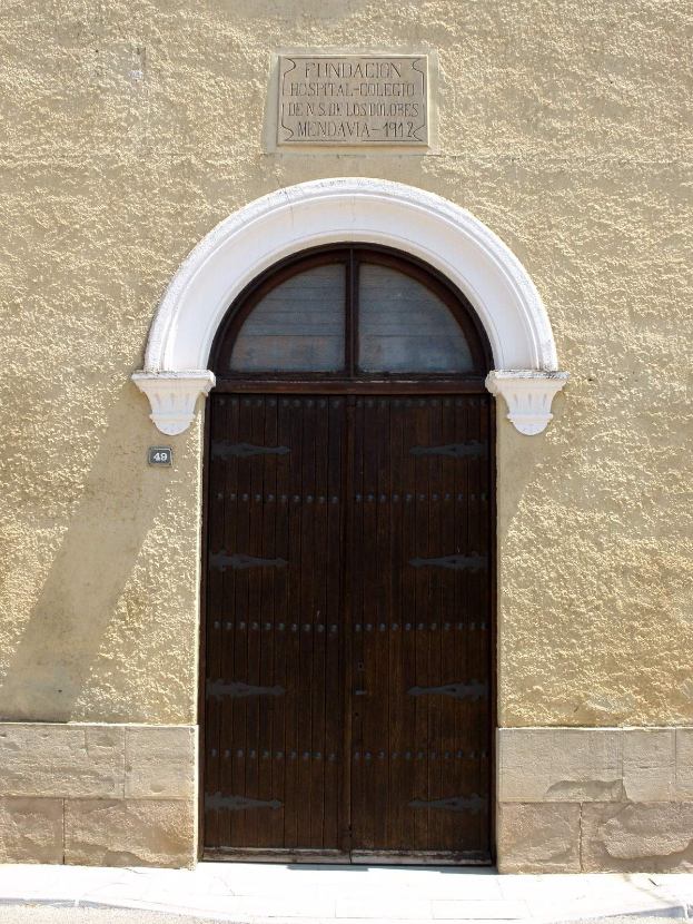 Alte hölzerne Tür mit einem Namensschild darüber, das wahrscheinlich einen Krankenhauseingang markiert, in einem steinernen Gebäude mit einer Straße unten.