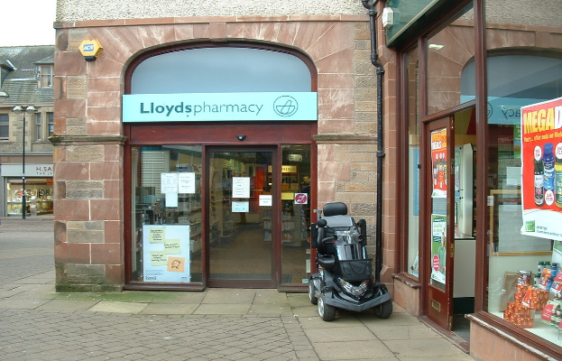 Eine Apothekenfiliale mit einem vor ihr geparkten Fahrzeug und einem Geb\344ude in der linken Ecke.