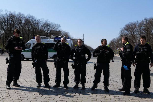 Gruppe von Polizeibeamten vor einem Rettungswagen auf einer Straße mit Bäumen, Laternen und einem klaren Himmel.