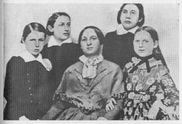 Schwarzes und weißes Foto einer vielfältigen Gruppe von Frauen mit einer sitzenden Frau in der Mitte, verbunden mit dem Text "Die Frauenwahlrechtsbewegung" unten.