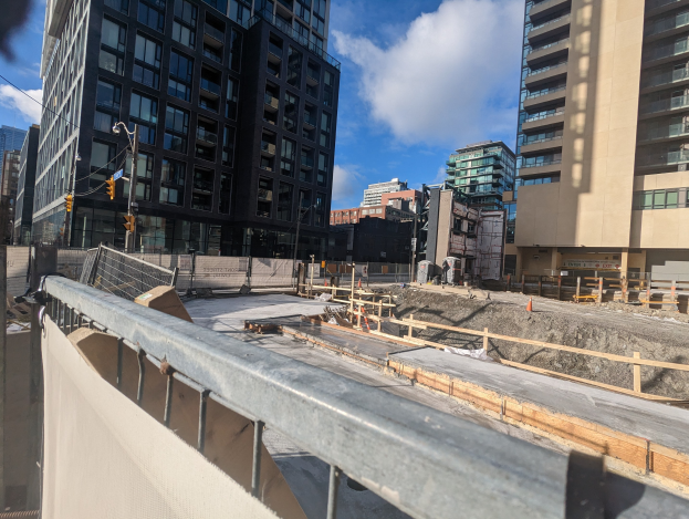 Baustelle in Toronto, Ontario mit einem großen Gebäude im Bau, umgeben von Absperrungen, Pfählen, Verkehrszeichen und Schildern, unter einem bewölkten Himmel.