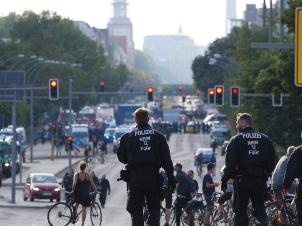 Eine Gruppe von Polizisten auf Fahrrädern auf einer von Bäumen gesäumten Straße mit Gebäuden und einem klaren blauen Himmel im Hintergrund.