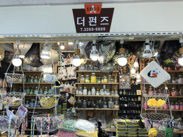 Ein unordentlicher Laden in Seoul mit verschiedenen Gegenständen wie Körben, Lampen, Flaschen und Spielzeugen auf Regalen, mit einem Schild oben, das anzeigt, dass es einer der besten koreanischen Läden ist.