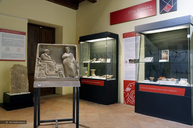 Ein Museumsraum in Rom, Italien, der verschiedene Kunstwerke zeigt, darunter Statuen auf Ständern, Glasvitrinen mit Gegenständen und informativen Texttafeln an den Wänden.