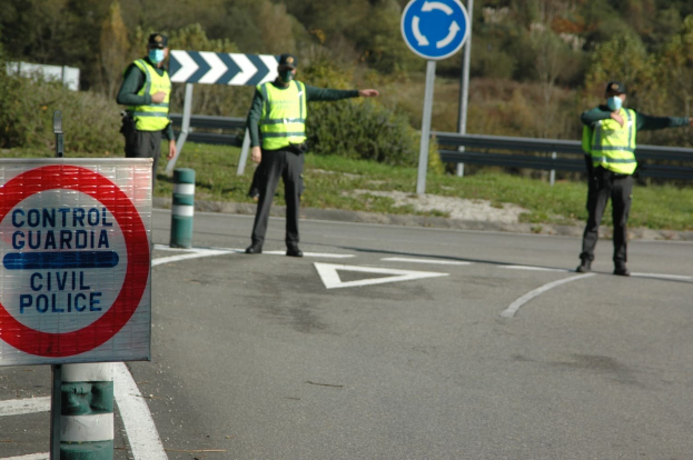 Drei Polizeibeamte in grünen Jacken und schwarzen Hosen stehen an einer Straßenrand bei Bäumen, einem Geländer, einem Verkehrsschild und einem Schuh.